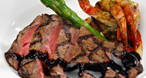 Sliced steak topped with a red wine reduction sauce, plated alongside fresh green asparagus spears and prawns.