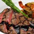 Sliced steak topped with a red wine reduction sauce, plated alongside fresh green asparagus spears and prawns.